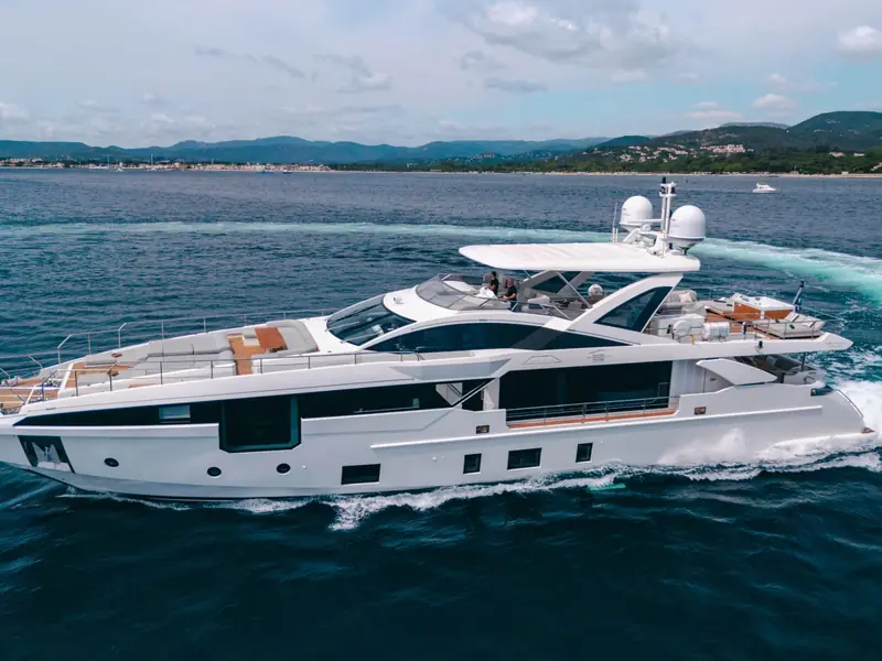 NEMESIS yacht cruising at speed showing its profile, flybridge, and satellite domes against a coastal backdrop.