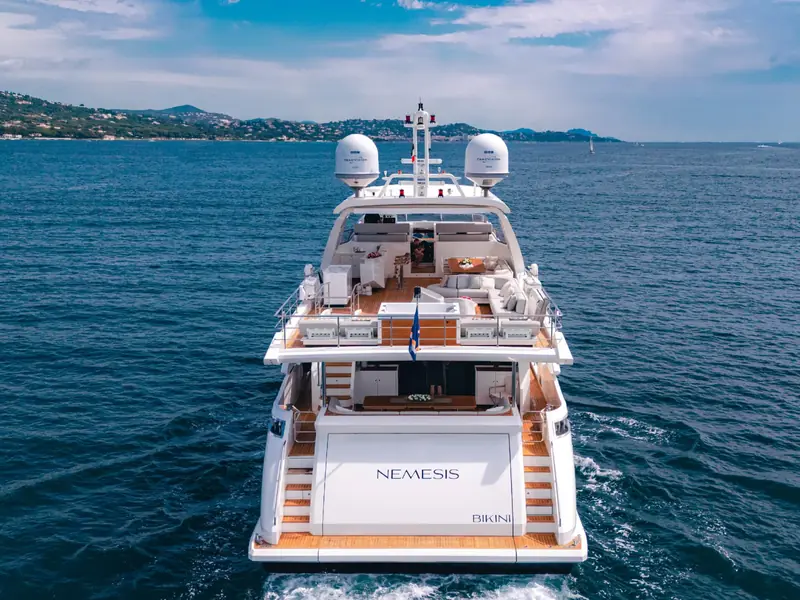 NEMESIS yacht stern view showing the flybridge, swim platform, and satellite domes while cruising at sea.