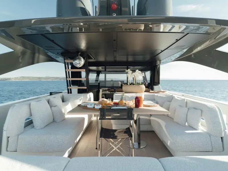 PETITCHET II yacht aft deck dining area with white sofas and a wooden table set for lunch.