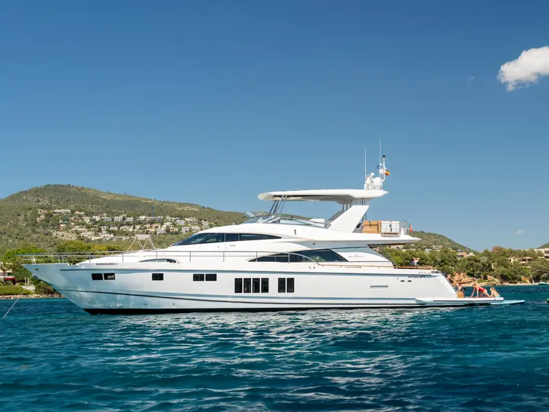 PAPAMARES motor yacht anchored in a bay with hills in the background, showing its profile and swim platform.