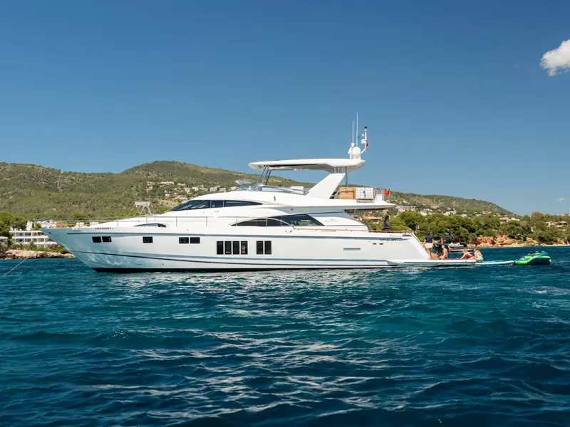 PAPAMARES yacht anchored in blue water with people on the swim platform and hills in the background.