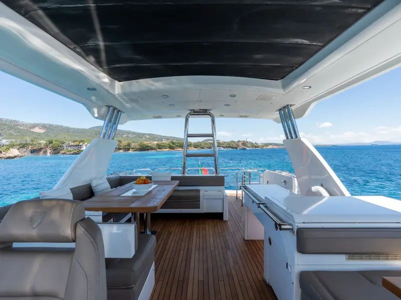 PAPAMARES yacht flybridge featuring a teak deck, dining table, and wet bar under a hardtop overlooking the sea.