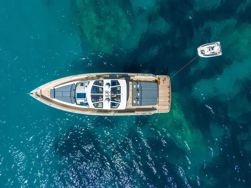 Top-down aerial view of yacht PETITCHET anchored in turquoise water with a small tender towed behind.