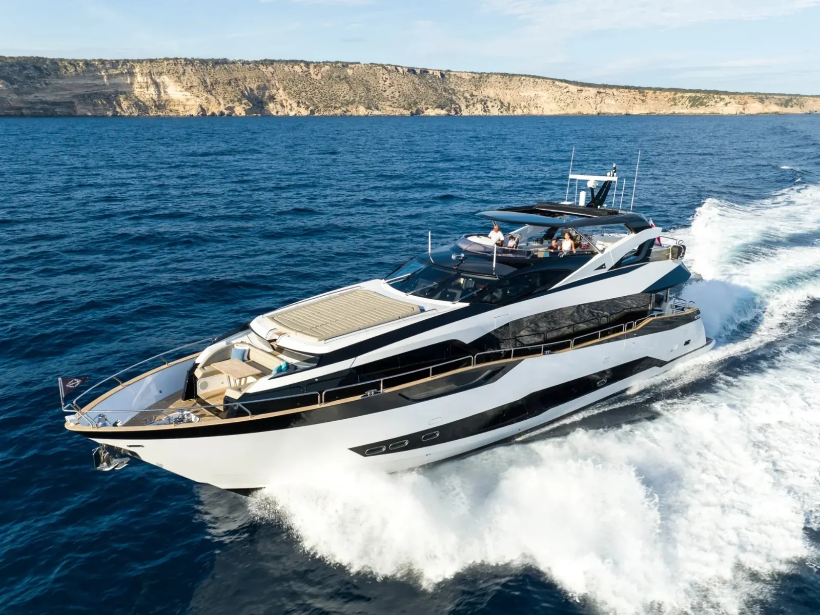 BLUE INFINITY ONE cruising at speed on the ocean with a rocky coastline in the background.