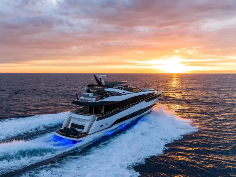 BLUE INFINITY ONE cruising at sunset with blue underwater lights and a white wake.