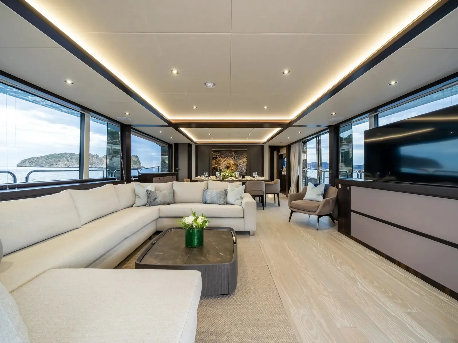 BLUE INFINITY ONE main salon with L-shaped white sofa, coffee table, and dining area looking out to sea.