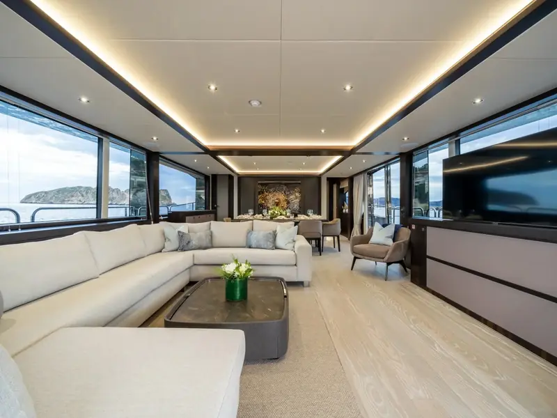 BLUE INFINITY ONE main salon with L-shaped white sofa, coffee table, and dining area looking out to sea.