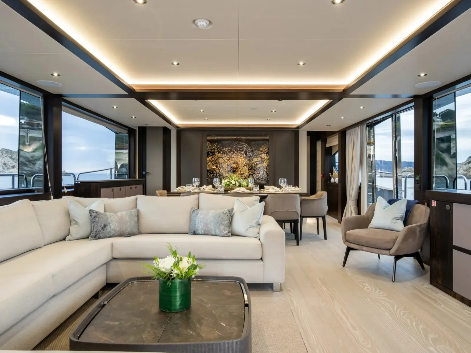 BLUE INFINITY ONE yacht salon featuring a white L-shaped sofa, coffee table, and dining area with large windows.