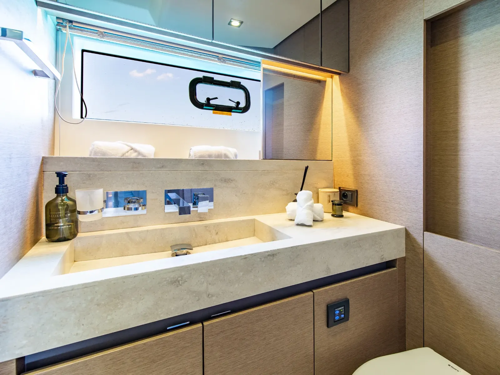 BLUE M yacht bathroom featuring a stone vanity, integrated sink, wooden cabinetry, and a digital control panel.