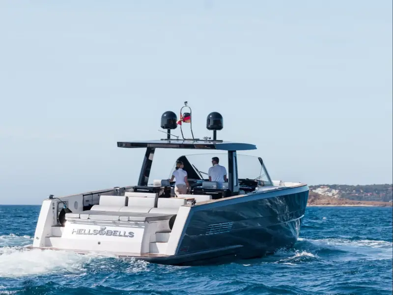 BOMBON, a Fjord 48 Open motor yacht, cruising at sea with two people at the helm and a large sunpad aft.