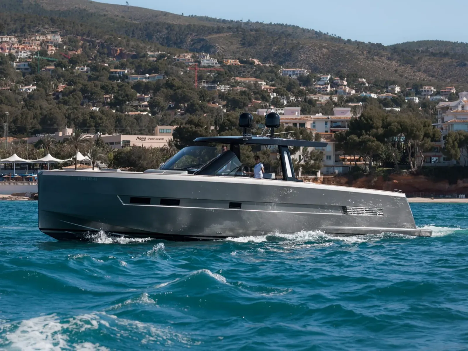 BOMBON motor yacht cruising at speed with a grey hull and black T-top near a hilly coastline.