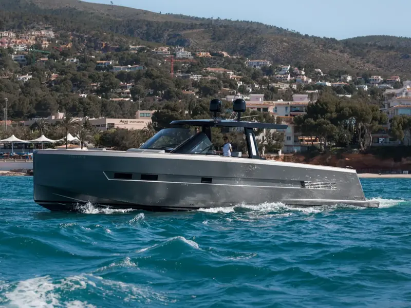 BOMBON motor yacht cruising at speed with a grey hull and black T-top near a hilly coastline.