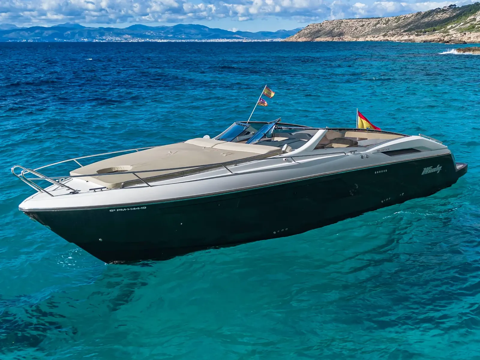 CUCA, a Windy 39 Camira motor yacht with a dark hull, anchored in clear turquoise water near a coastline.