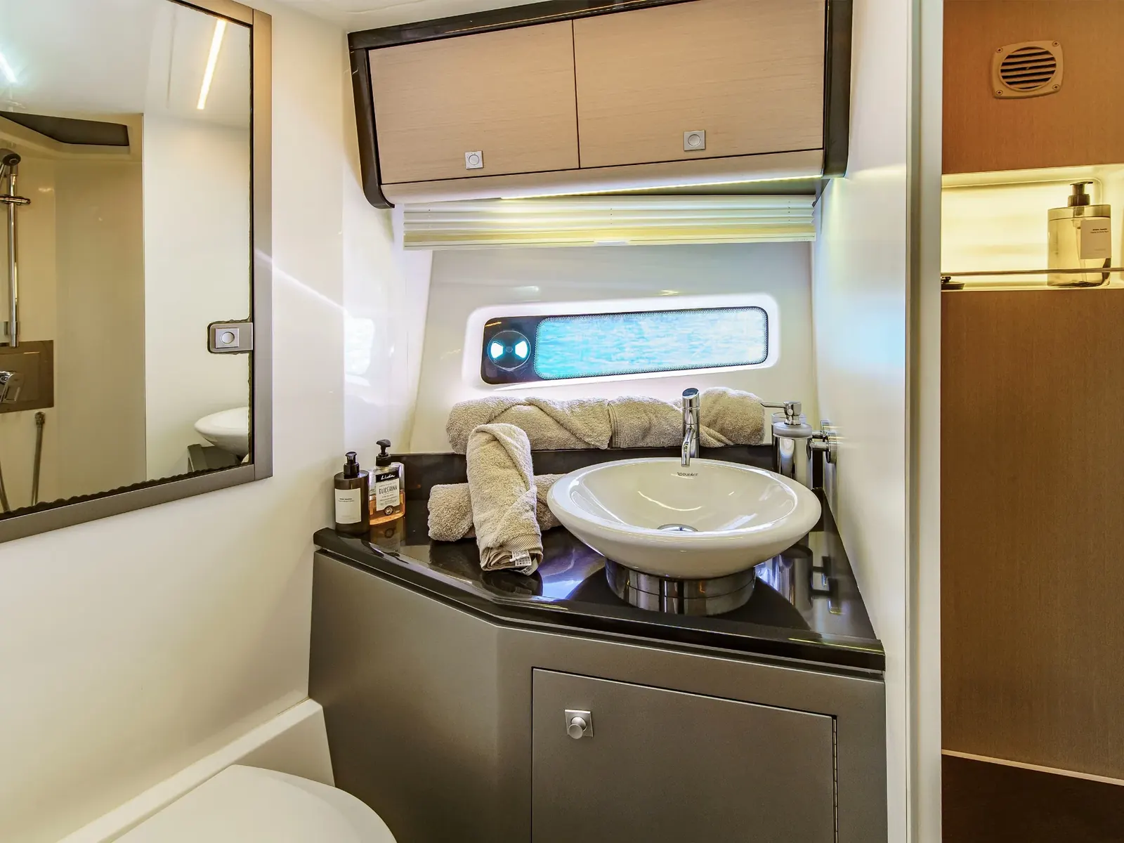 CUCA yacht bathroom featuring a white vessel sink, dark countertop, and wooden cabinetry.