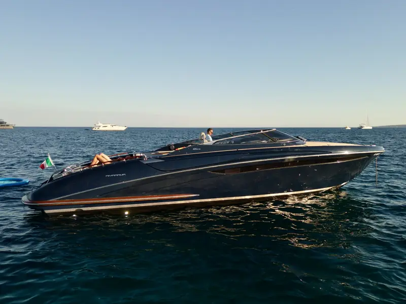 JAD & JULIA, a dark blue Riva 44 Rivarama motor yacht, anchored on calm water at sunset.