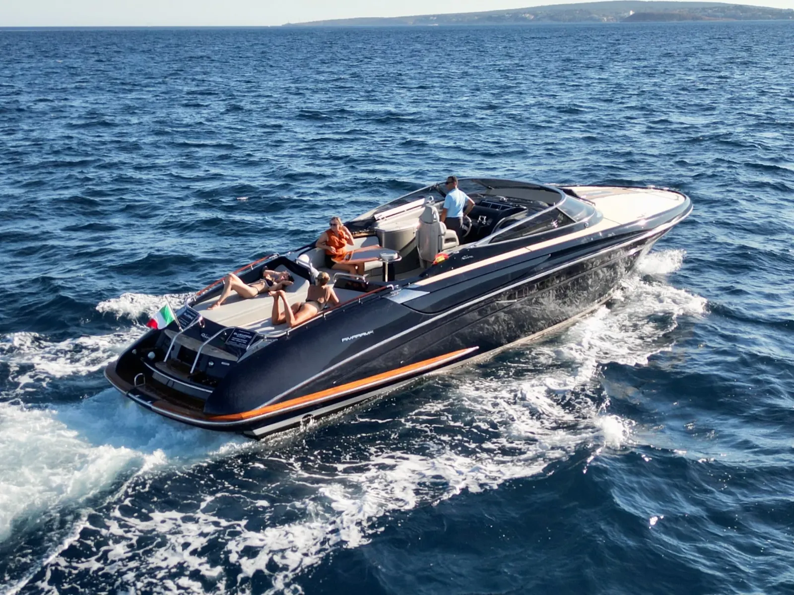 JAD & JULIA yacht cruising on open water with people on the aft sunpad and at the helm.