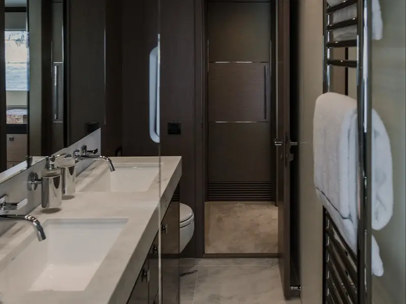 LADY M yacht bathroom featuring double sinks, marble vanity, and a heated towel rail.