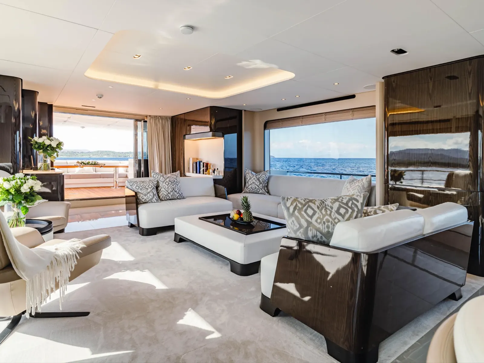 NEMESIS yacht salon featuring white sofas, dark wood paneling, and large windows overlooking the sea.
