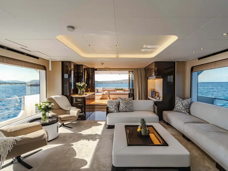 NEMESIS yacht salon interior featuring white sofas, large windows with sea views, and a tray with fruit.