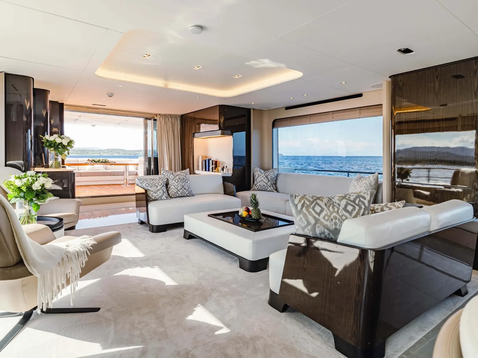 NEMESIS yacht salon interior featuring white sofas, dark wood paneling, and large windows overlooking the sea.