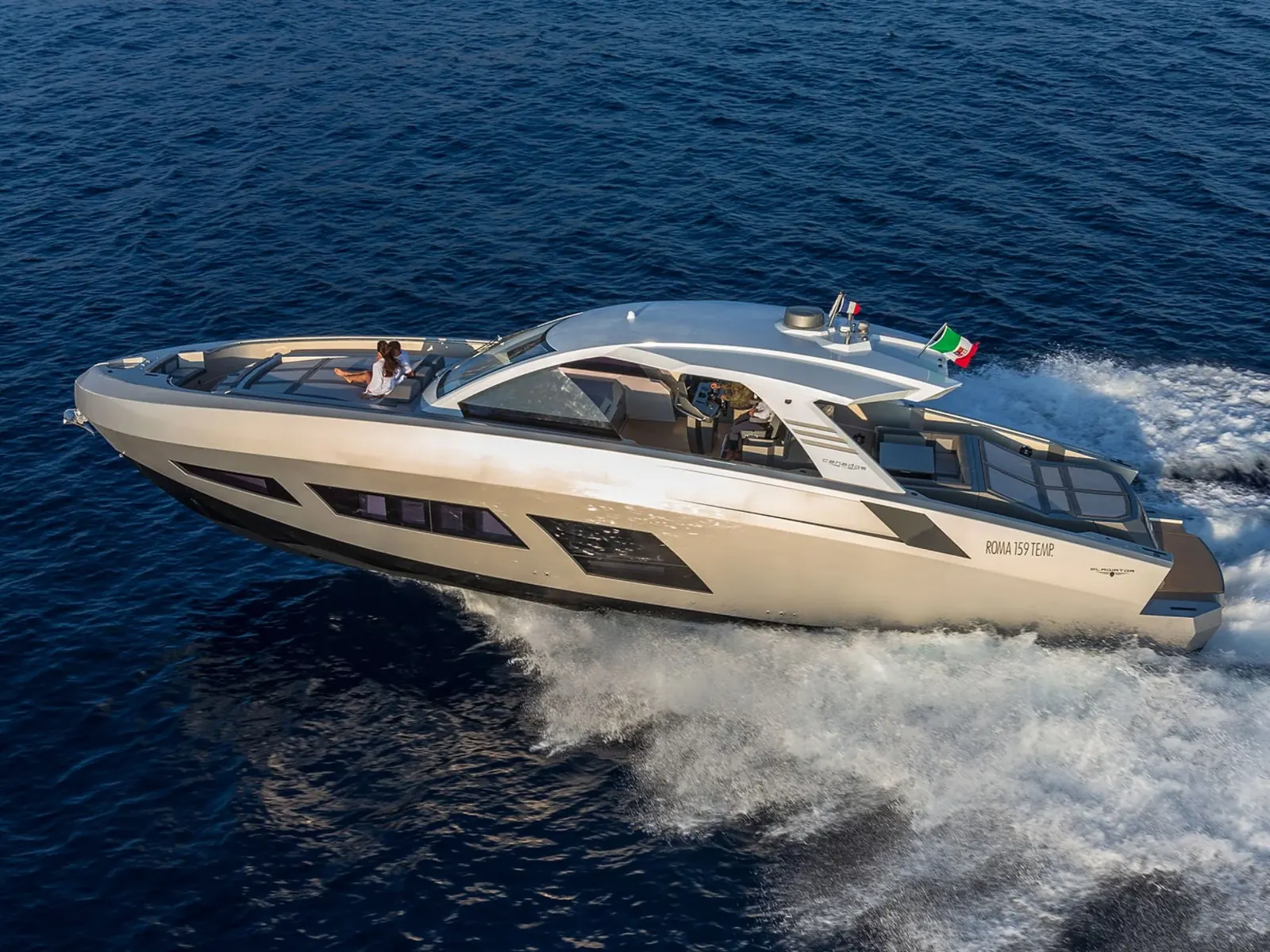 Aerial profile of the yacht NEXT cruising at high speed on blue water with two people on the foredeck sunpad.