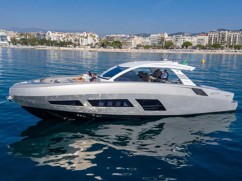 Profile view of the motor yacht NEXT anchored in calm blue water with people on the foredeck sunpad.