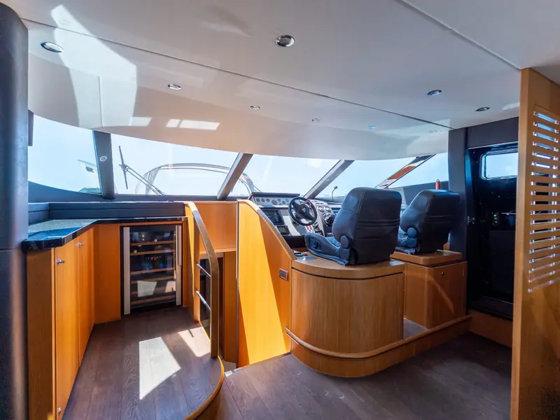 Interior helm station of PAPAMARES with two black leather seats, wood cabinetry, and a wine cooler.