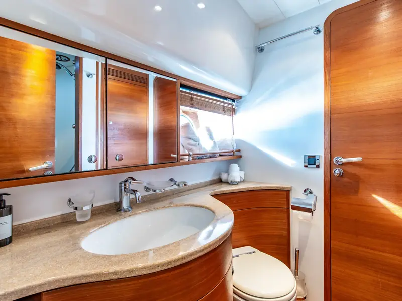 PARODIA yacht bathroom featuring a wood-paneled vanity, marble countertop, oval sink, and mirror cabinets.