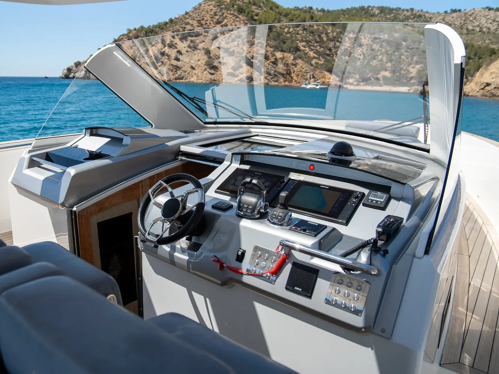 PETITCHET yacht helm station with Raymarine displays, joystick, and steering wheel overlooking a coastal cove.