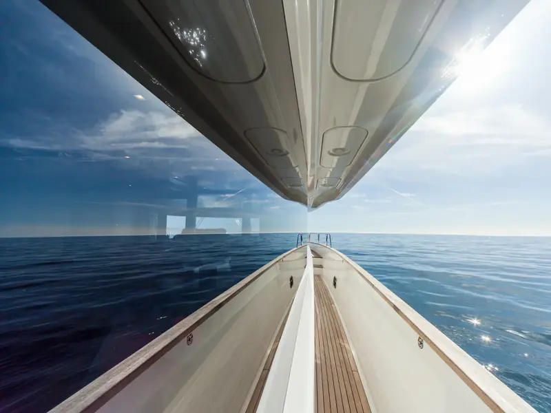 SALACIA yacht side deck view showing teak walkway, large reflective hull windows, and the bow pointing to open sea.