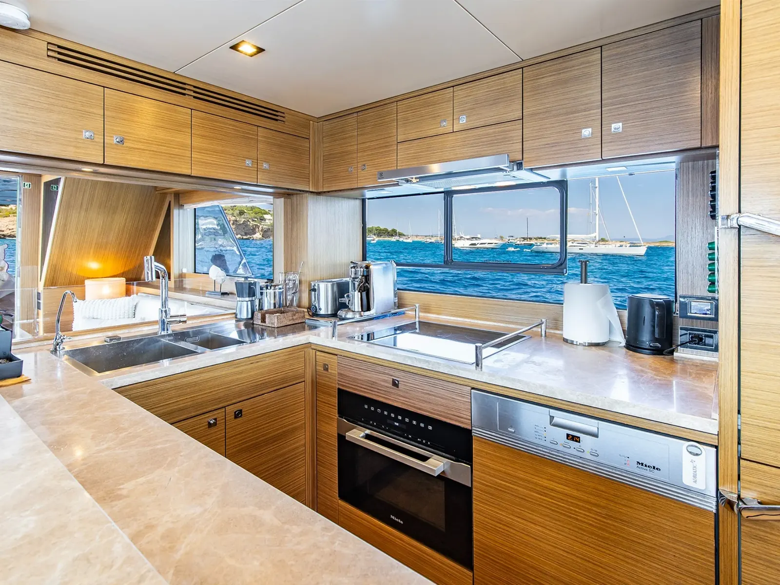Pantry der Yacht SALACIA mit Miele-Geräten, Holzschränken und Blick durch ein großes Fenster aufs Meer.