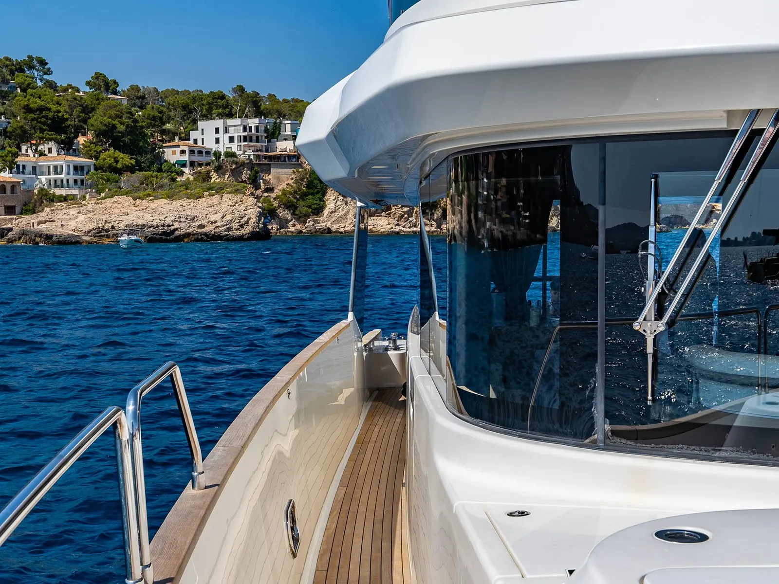SALACIA yacht side deck looking forward towards the bow with a view of a rocky coastline.