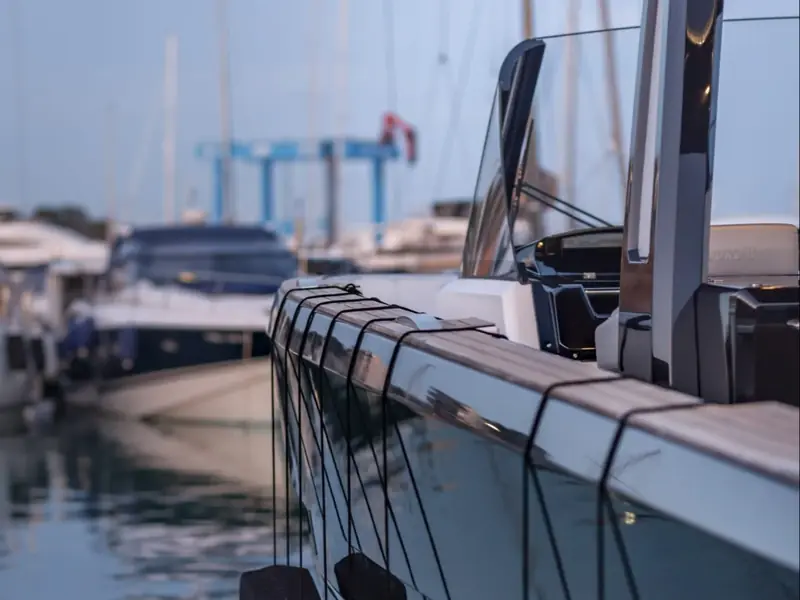 BOMBON yacht detail showing the teak gunwale, black hull reflection, and windshield in a marina.
