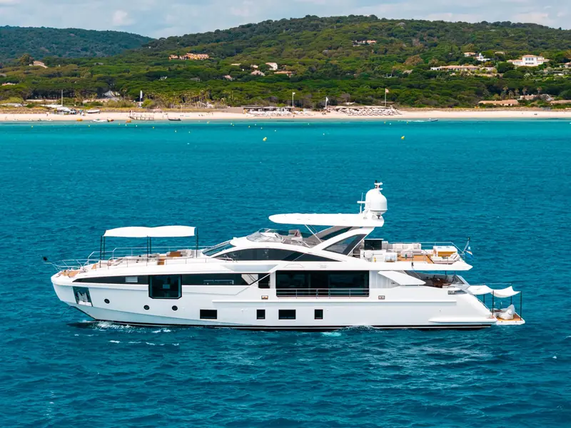 NEMESIS yacht profile cruising in blue water near a beach with a white hull and multiple decks.