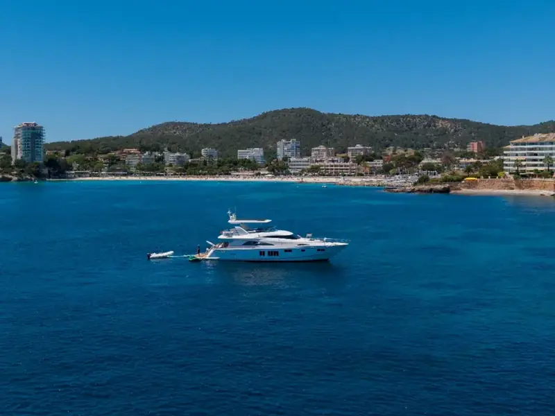PAPAMARES motor yacht anchored in a blue bay with a small tender at the stern and a coastal town in the background.