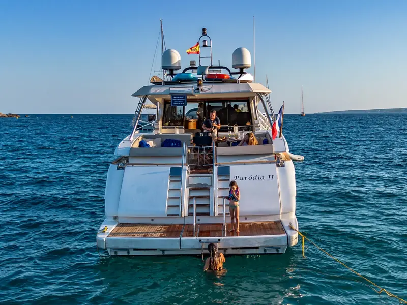 PARODIA yacht stern view showing the swim platform, aft deck seating, and satellite domes at anchor.