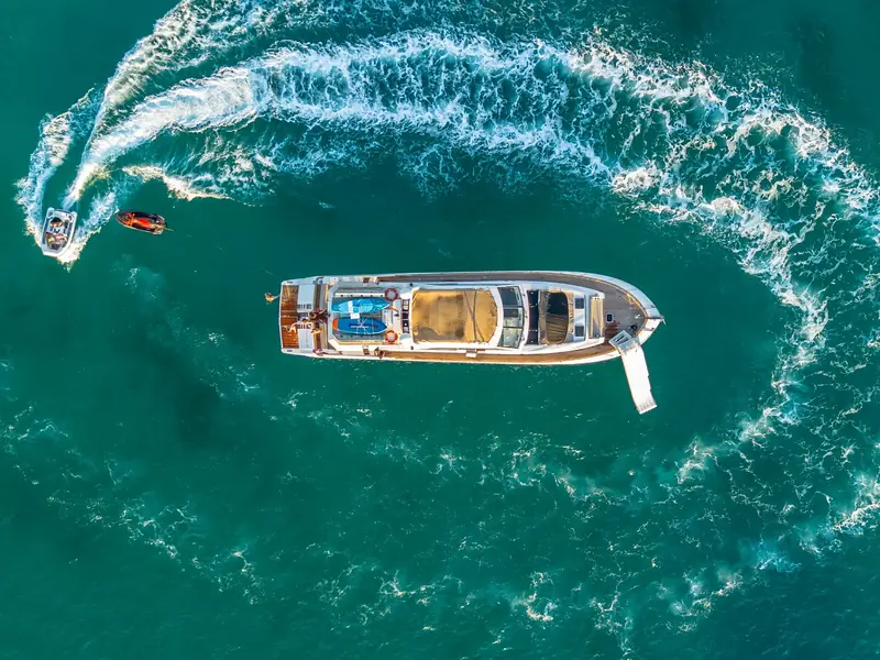 Aerial top-down view of PARODIA at anchor with a tender, jet ski, and inflatable slide deployed.