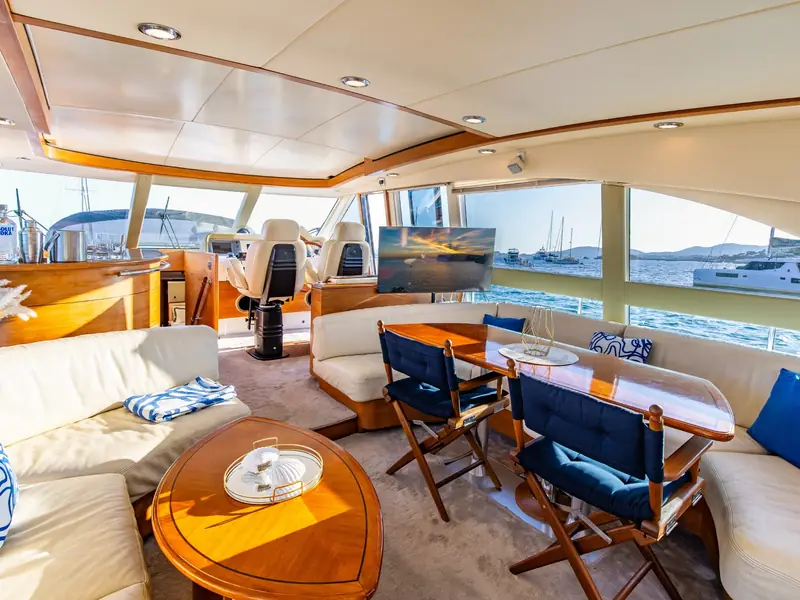 PARODIA yacht interior salon featuring a wooden dining table, white leather sofas, and a view of the helm station.