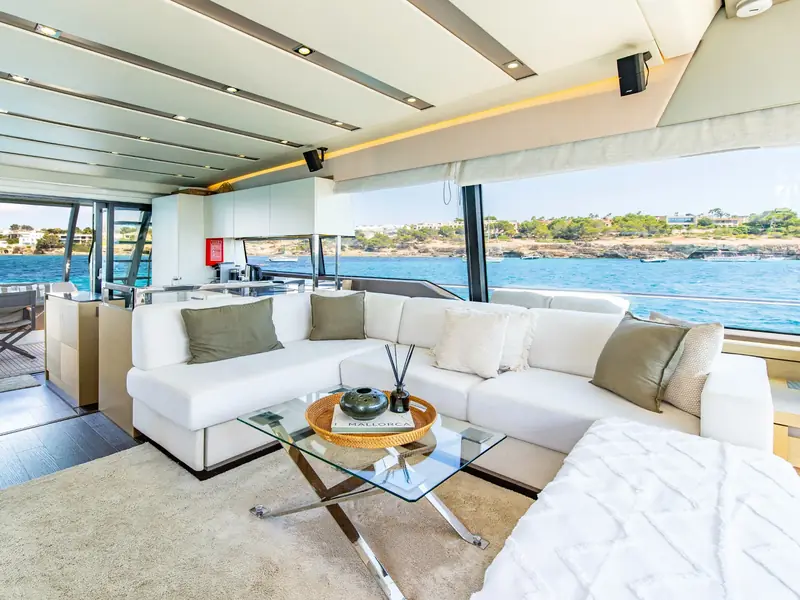 Interior salon of BLUE M featuring a white L-shaped sofa, glass coffee table, and large windows overlooking the sea.