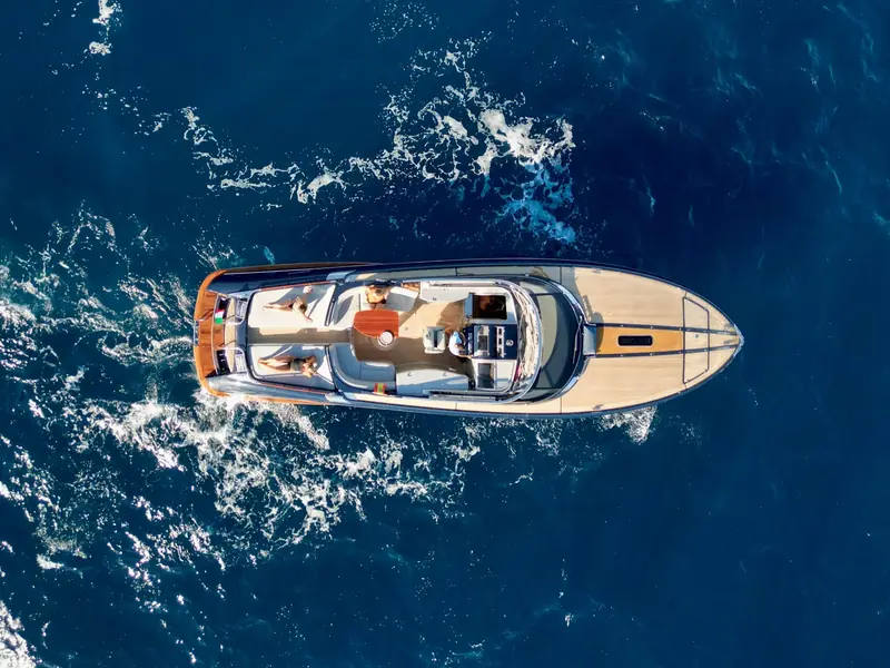 Aerial top-down view of JAD & JULIA cruising on blue water with people sunbathing on the aft deck.