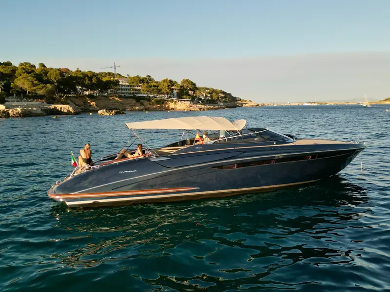 JAD & JULIA, a blue Riva 44 Rivarama motor yacht anchored in a bay with people on the aft sunpad.