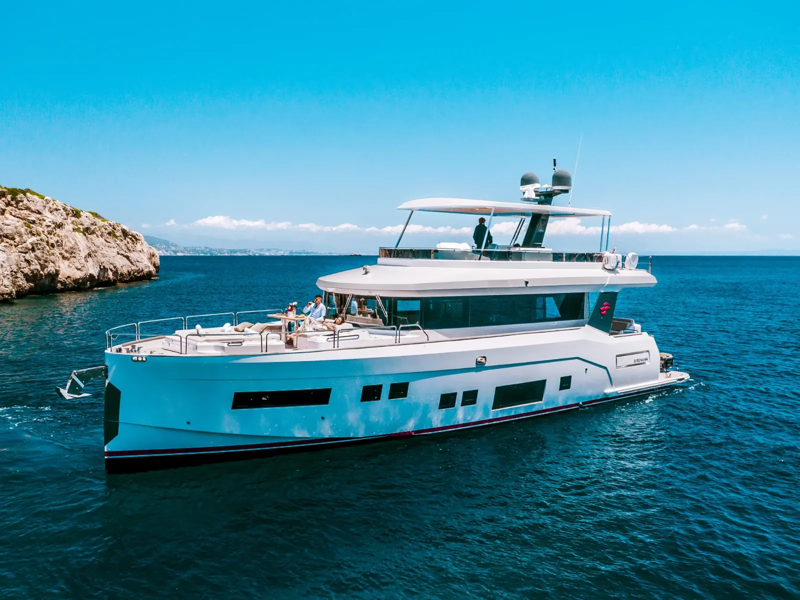 SALACIA motor yacht anchored in calm blue water near a rocky cliff under a clear sky.