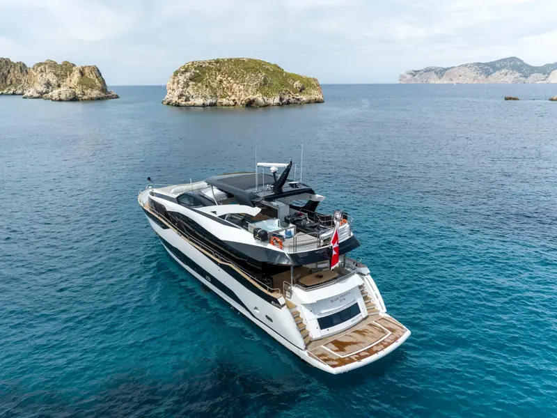 Aerial rear view of BLUE INFINITY ONE anchored in blue water near rocky islands.