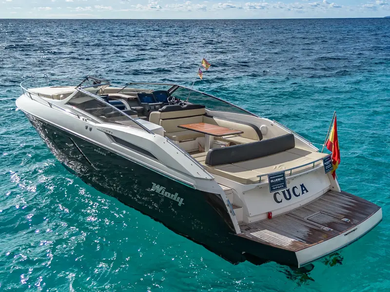 CUCA, a Windy 39 Camira motor yacht with a dark hull and teak swim platform, anchored in clear blue water.