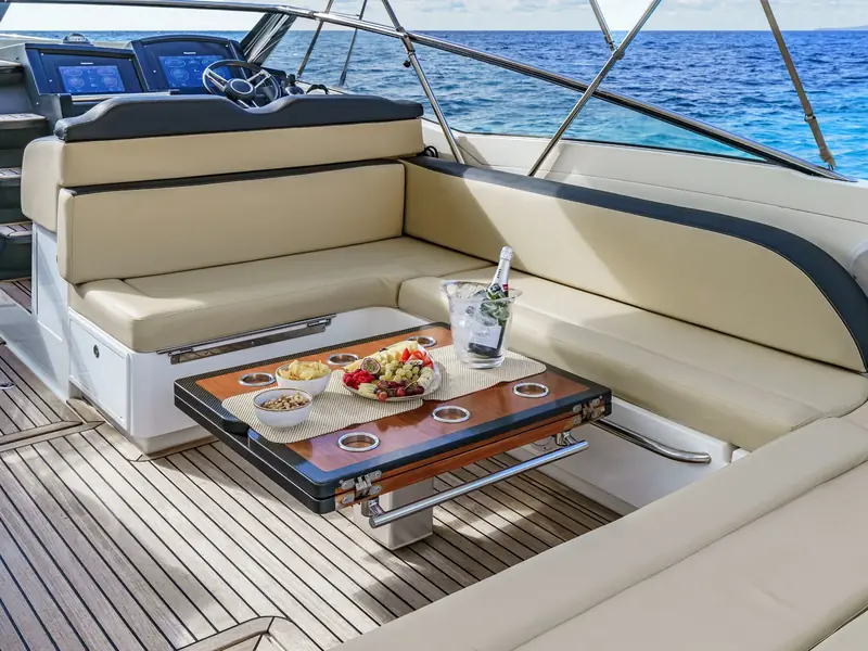 CUCA yacht aft deck seating area with a wooden table, snacks, and helm station visible in the background.