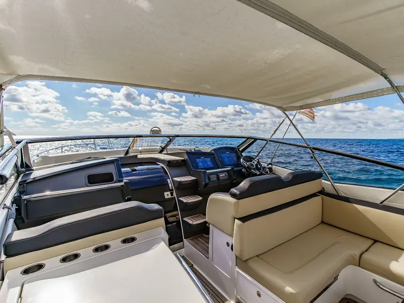 CUCA yacht helm station with dual displays, steering wheel, and tan seating under a bimini top at sea.